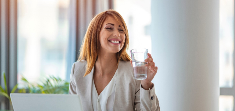 makrogol na zaparcia – uśmiechnięta kobieta przy biurku pijąca wodę